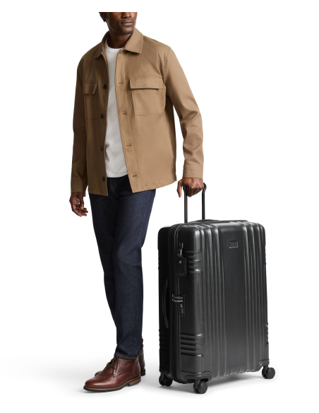 Valise soute extensible TUMI Latitude 76 cm Carbon Black, valise noire présentée à côté d’un voyageur