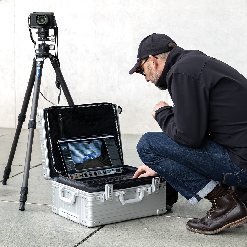 Photographe auprès d’une valise photo ALEON en aluminium ouverte et d’un appareil sur trépied