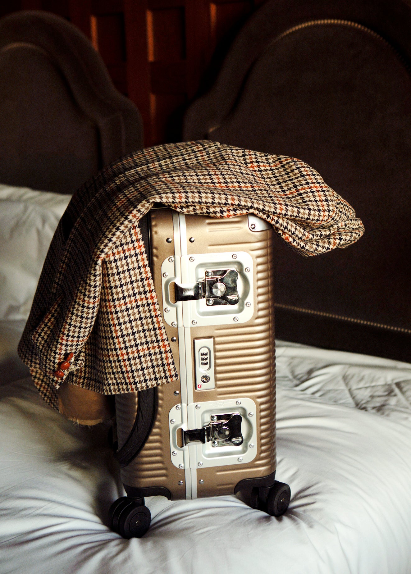 Valise FPM BANK LIGHT posée sur un lit, avec ses fermoirs papillon et sa coque nervurée visibles