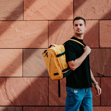 Voyageur portant un sac à dos American Tourister Take2Cabin jaune.