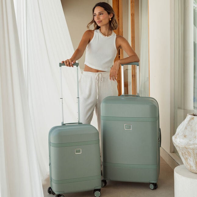 Deux valises Samsonite Image vert Thyme accompagnent une voyageuse dans une chambre.